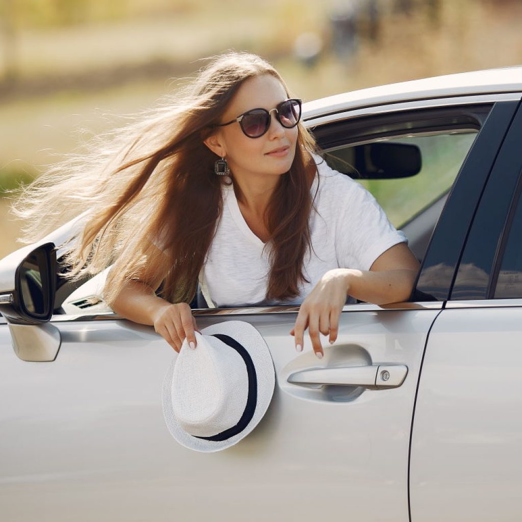 Woman by the car. Lady in a white t-shirt. Famale in a white hat.
